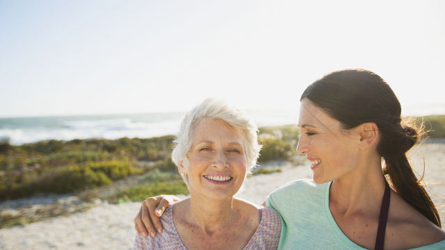 Zwei Frauen, Arm in Arm, lächeln am Strand bei sonnigem Wetter