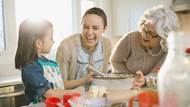 Fröhliche Familie beim Backen: Kind, Mutter und Großmutter lachen in einer sonnigen Küche